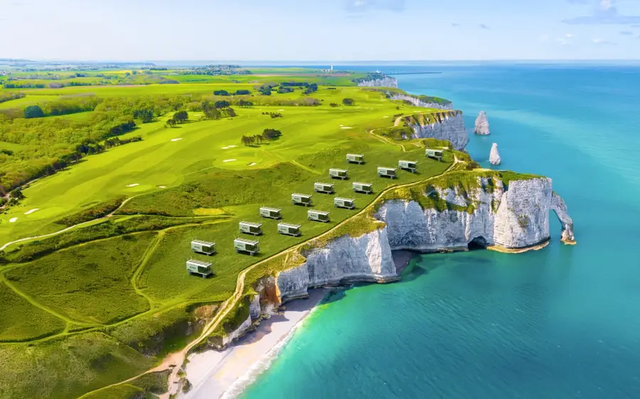 Cabins on a green coastal clifftop above turquoise sea